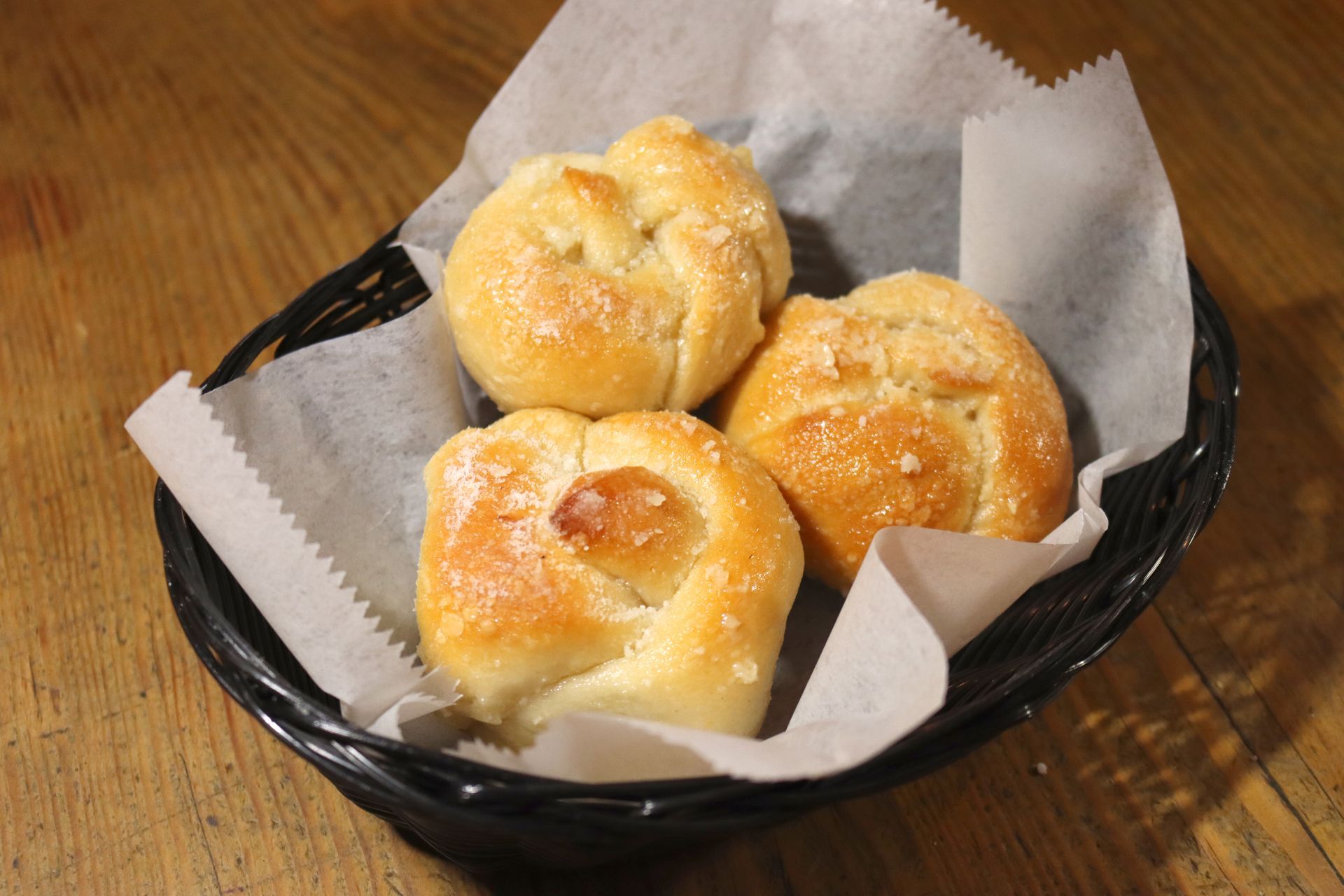 Three garlic knots are in a basket on a wooden table.
