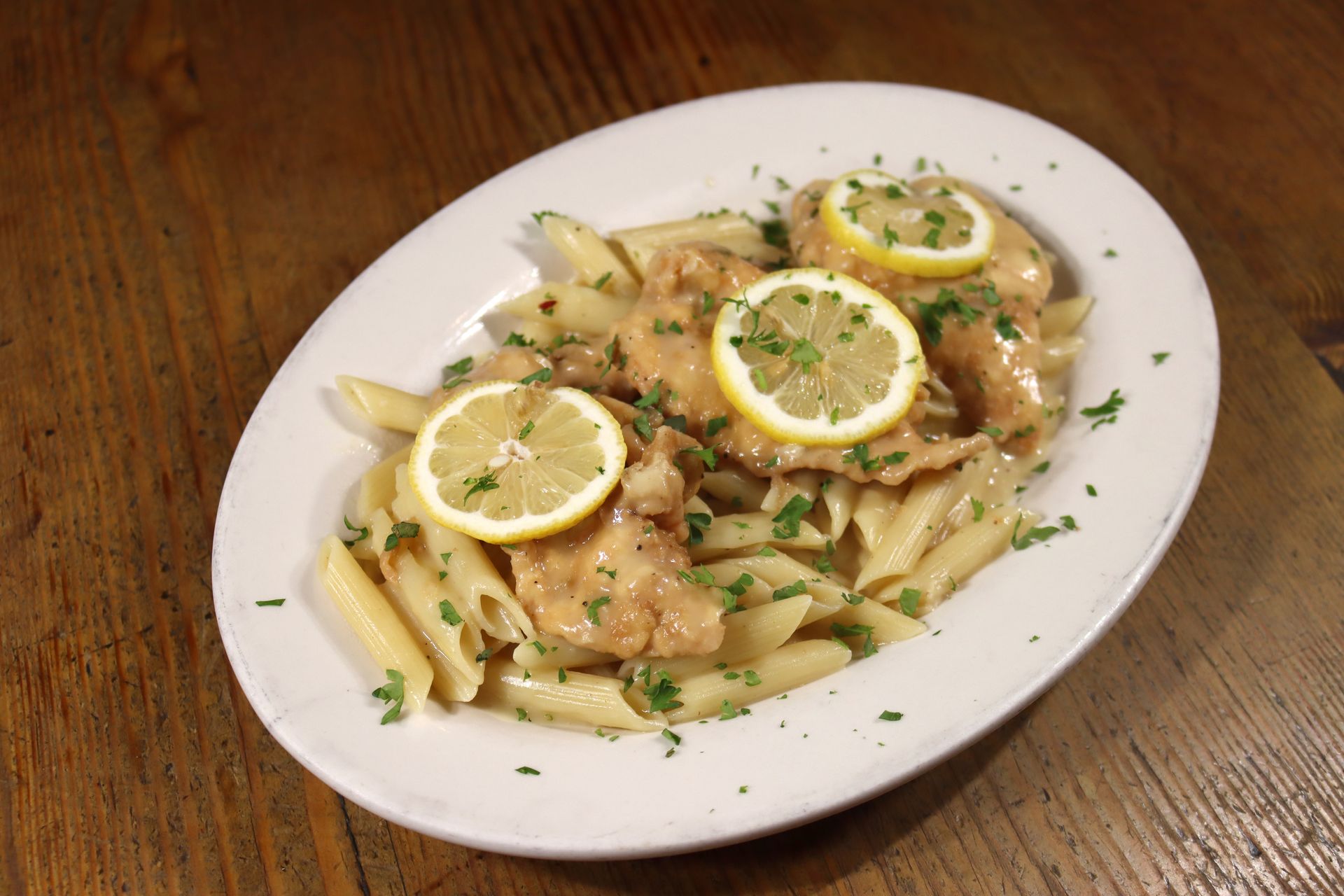 A white plate topped with pasta and lemon slices on a wooden table.