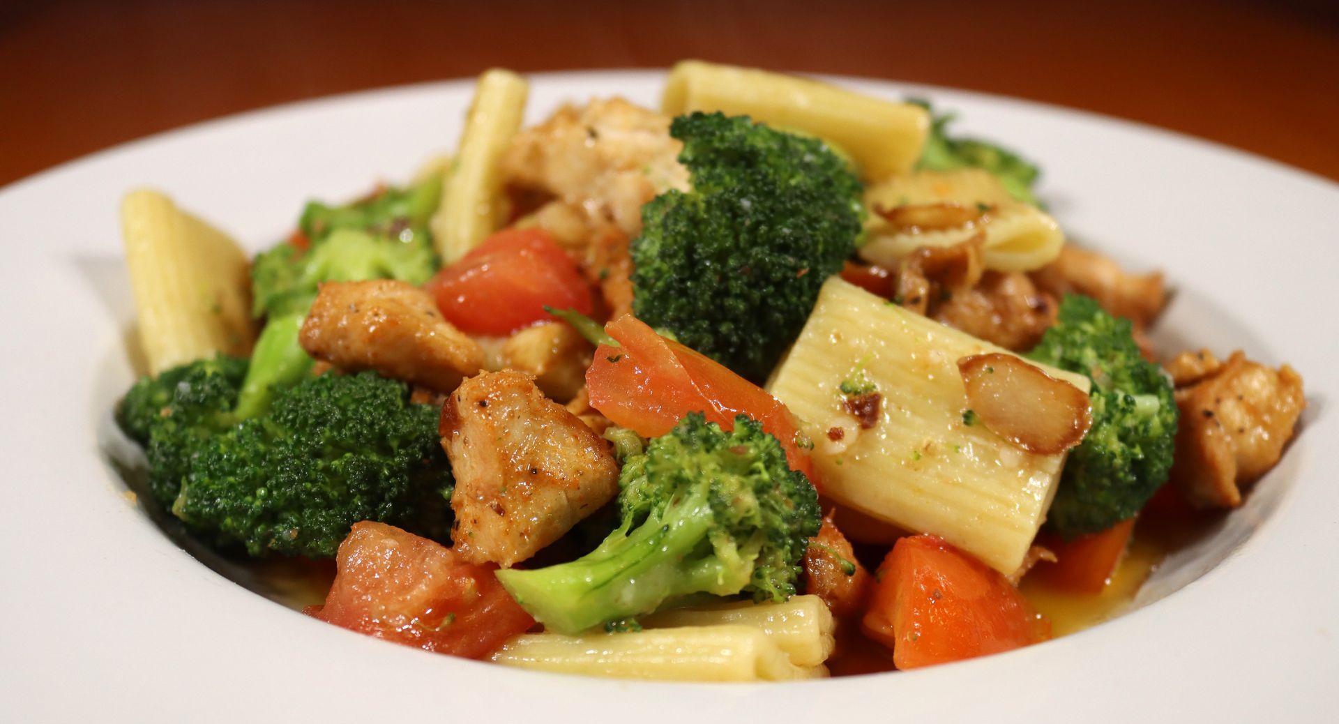 A white plate topped with pasta , broccoli , carrots and chicken.