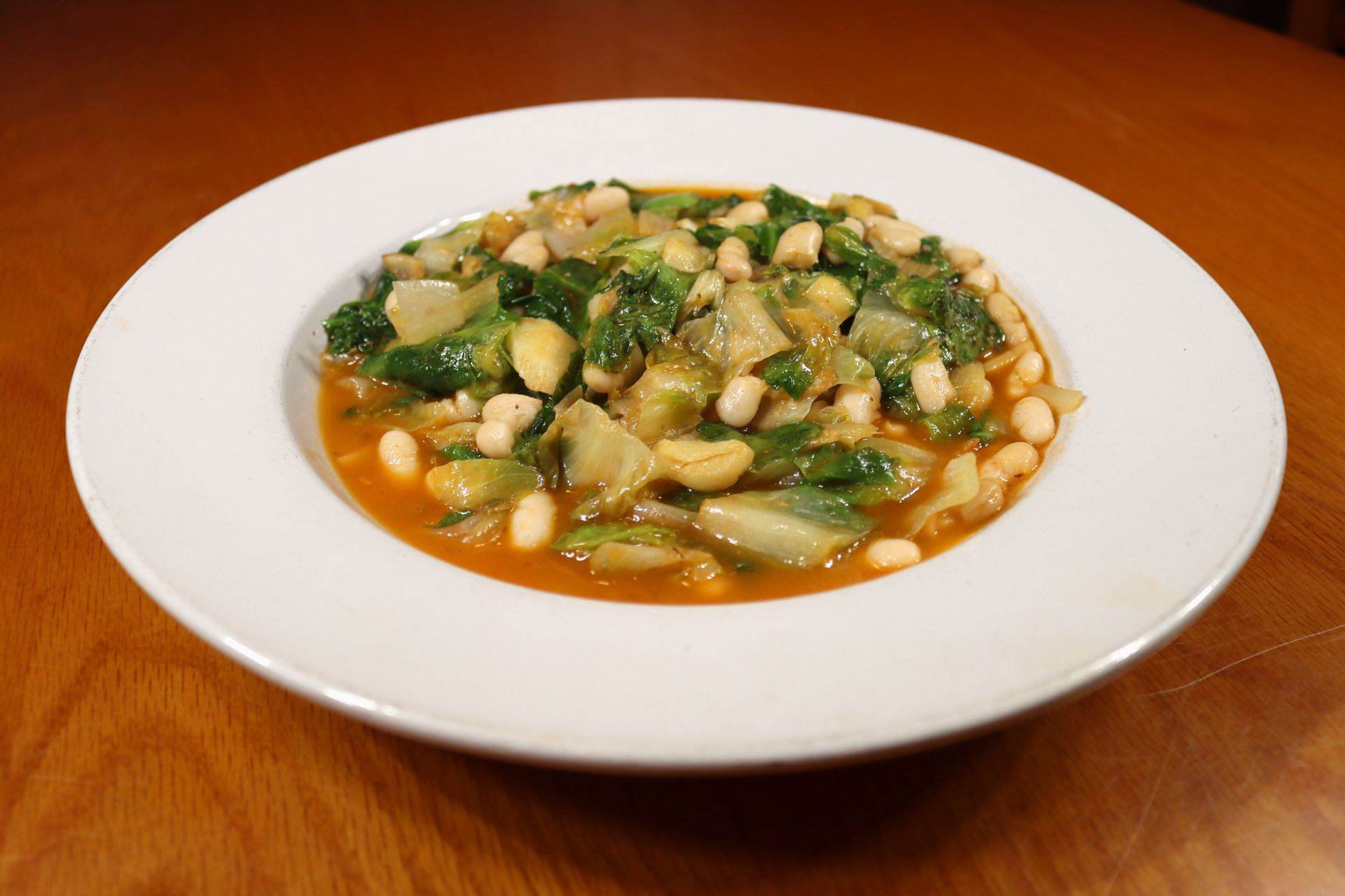 A white bowl filled with beans and vegetables on a wooden table.