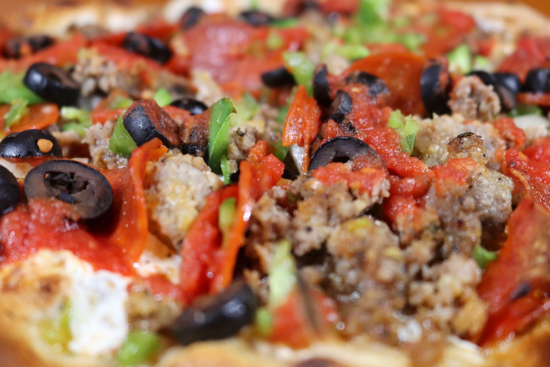A close up of a pizza with pepperoni , olives , tomatoes and cheese.
