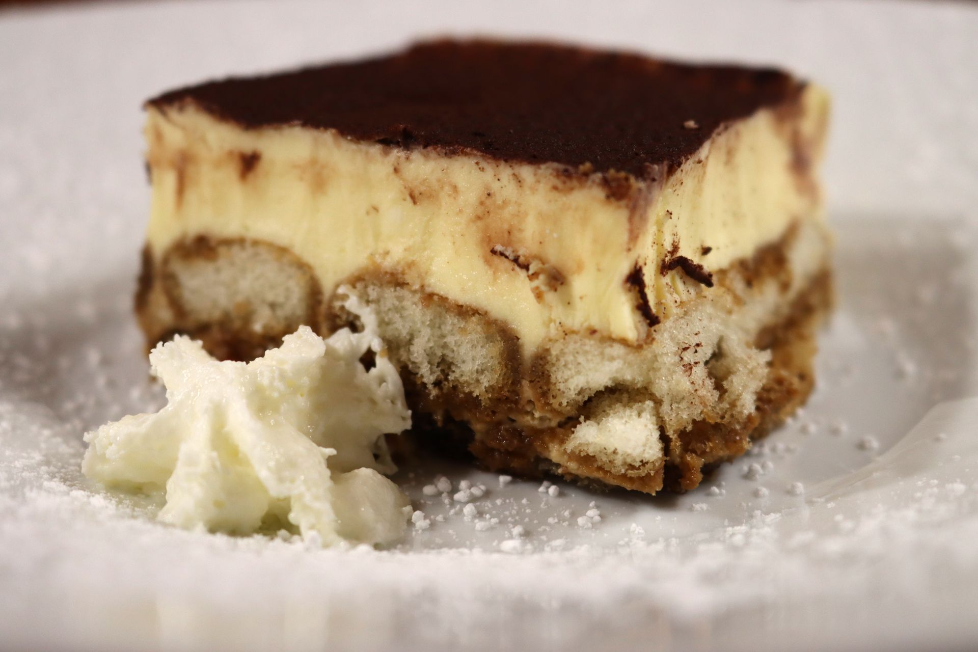 A piece of tiramisu with whipped cream on a white plate.