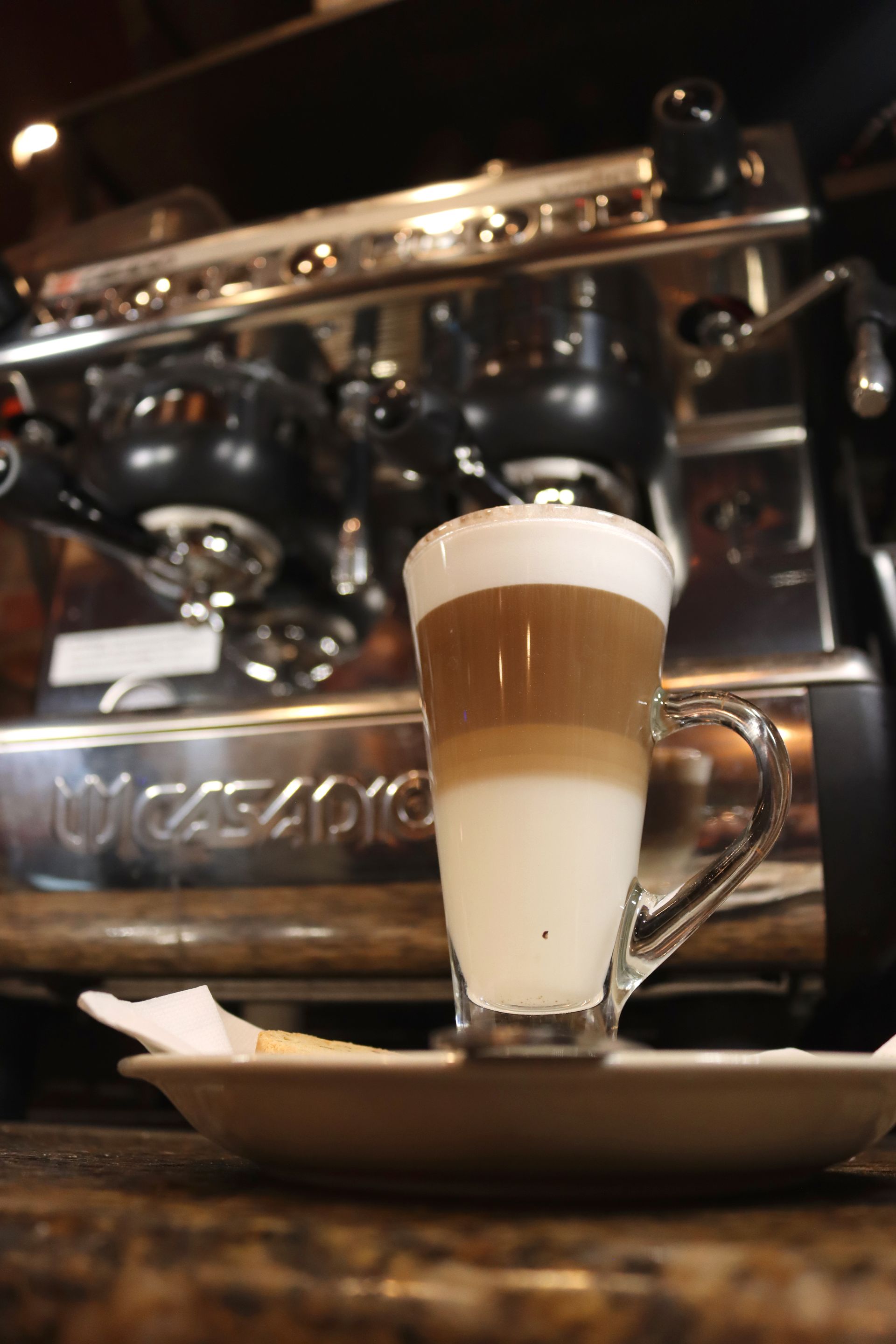 A cup of latte is on a saucer in front of a coffee machine