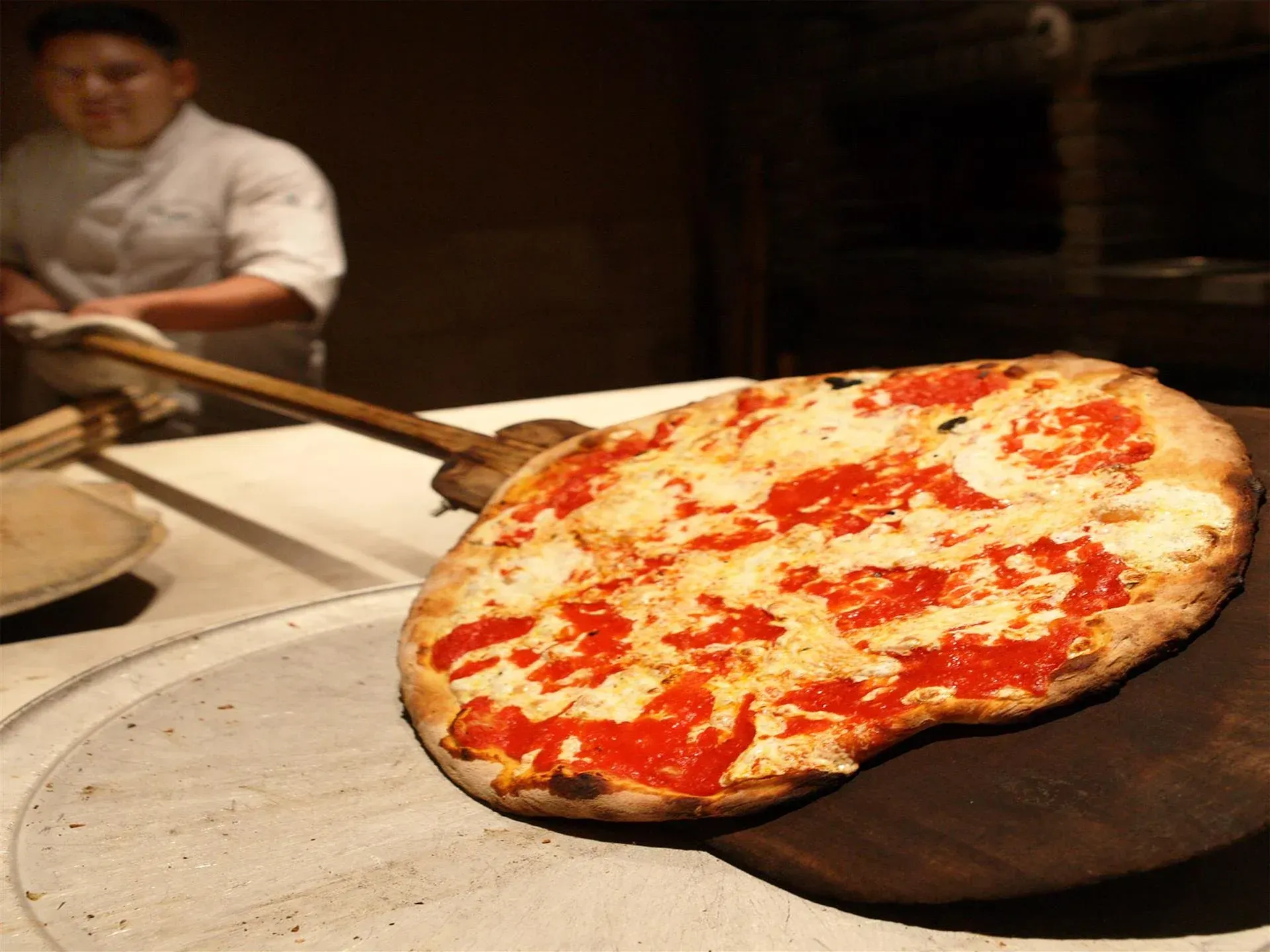 A pizza is being scooped out of the oven on a wooden paddle