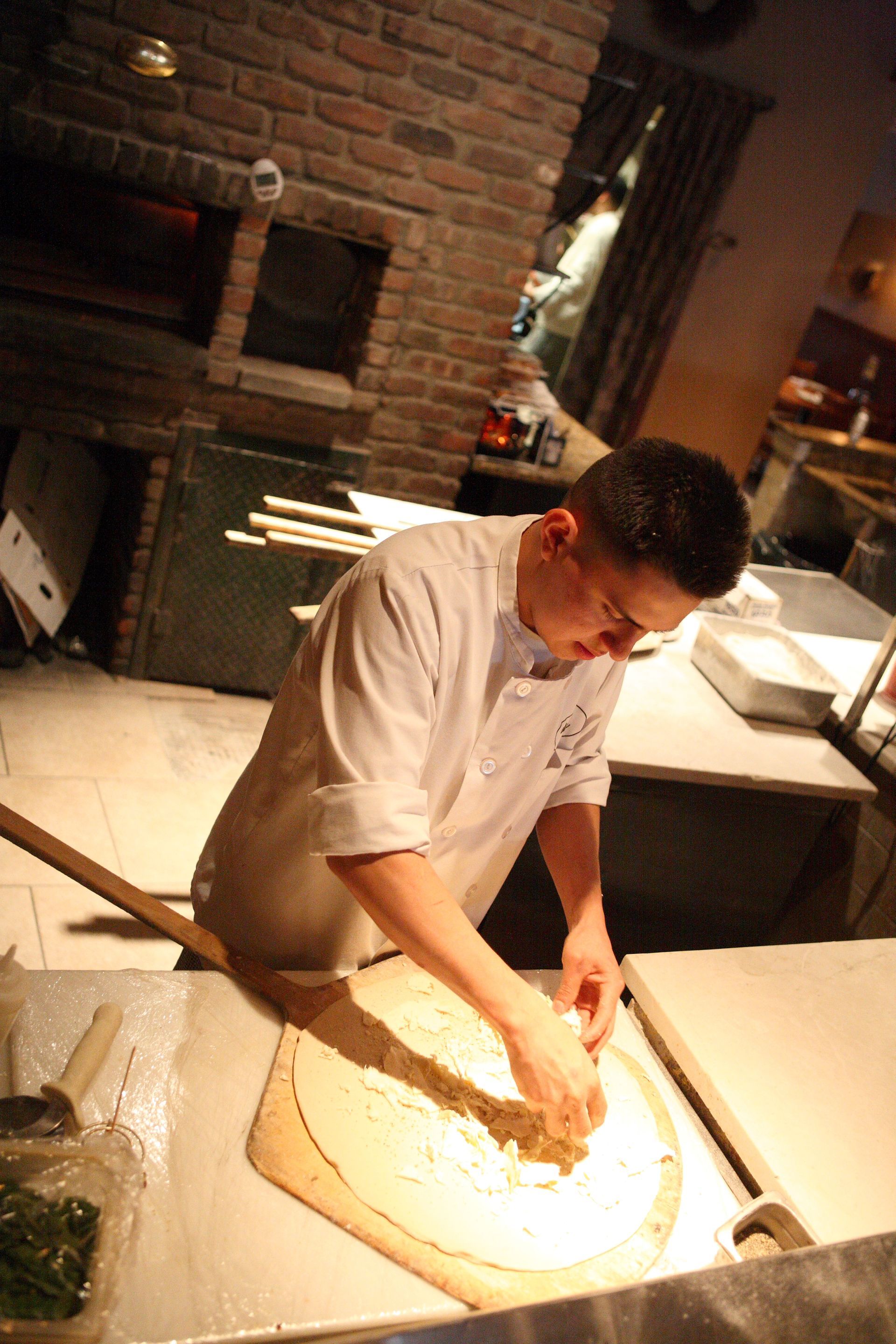 A man is rolling out pizza dough in a kitchen