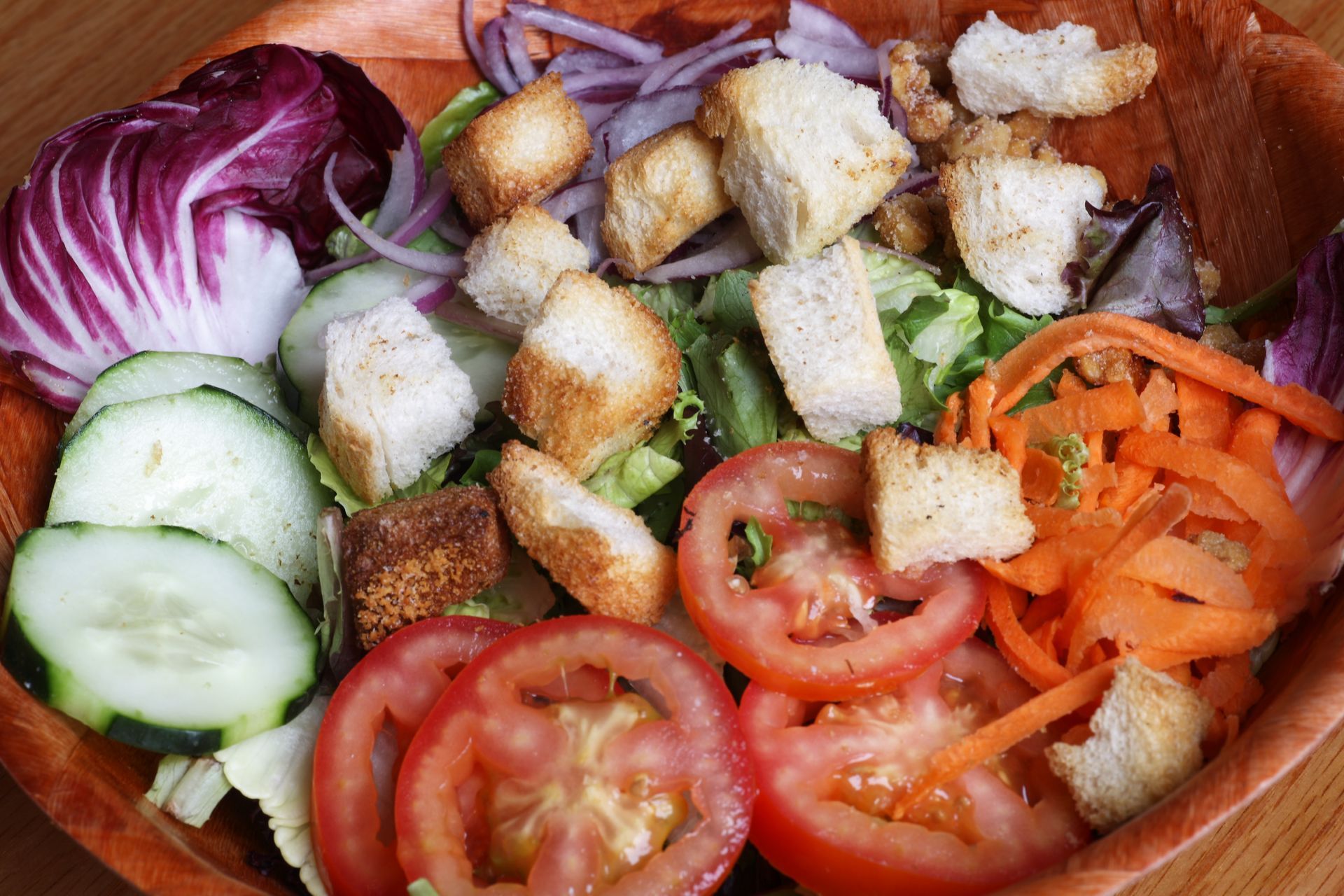 A wooden bowl filled with vegetables and croutons on a table.
