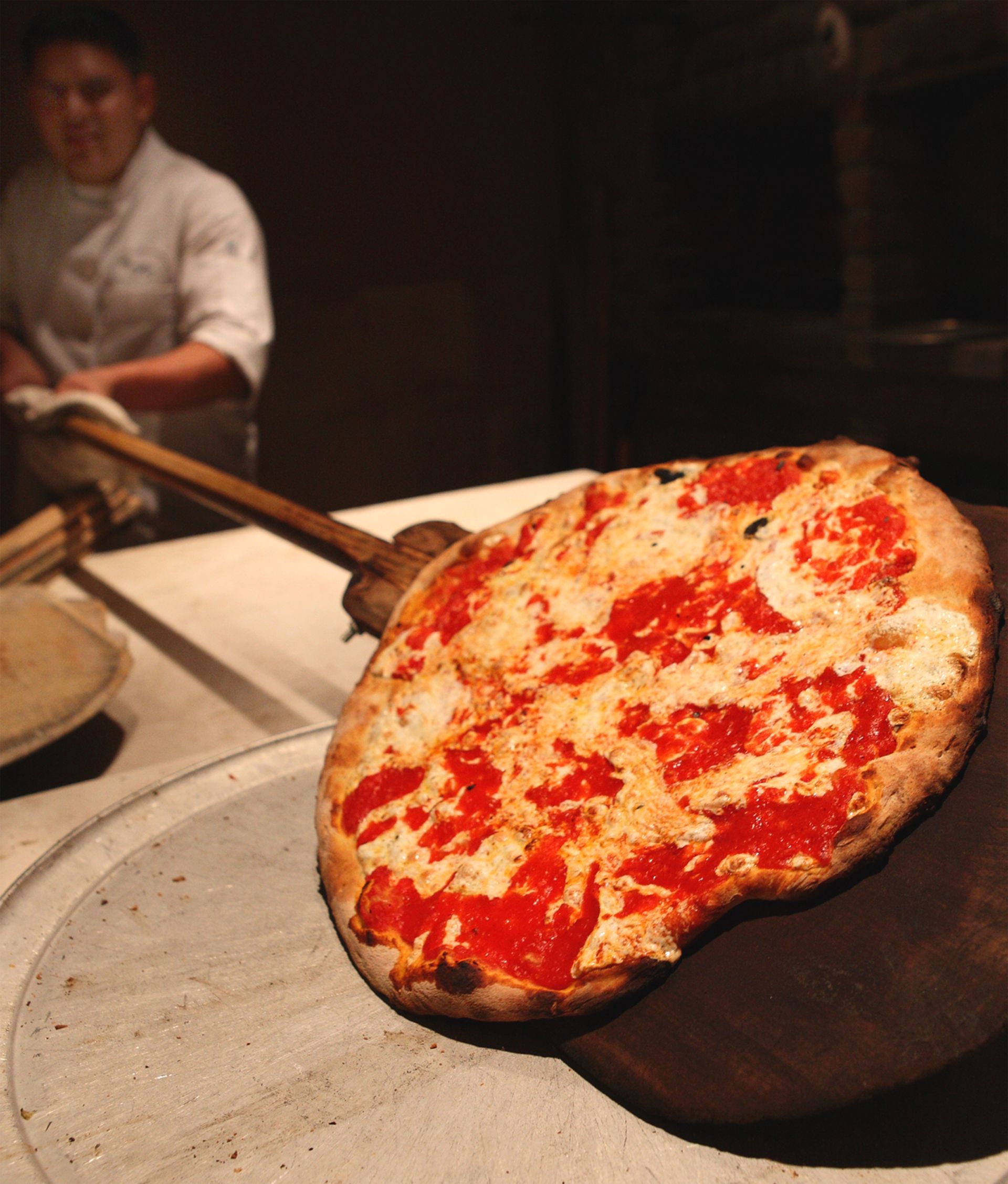 A pizza sitting on a wooden peel with a chef in the background