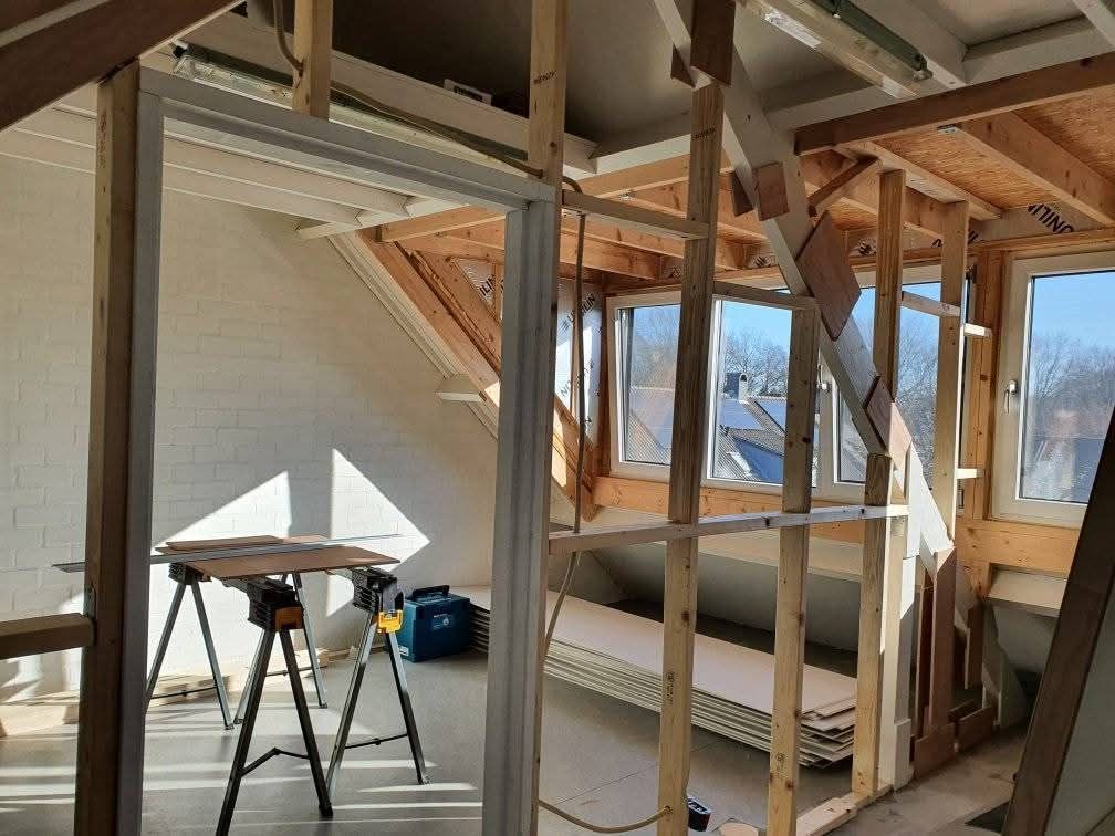 Interieurfoto van een kamer met zichtbare houten balken en ramen, een deuropening en een werktafel.