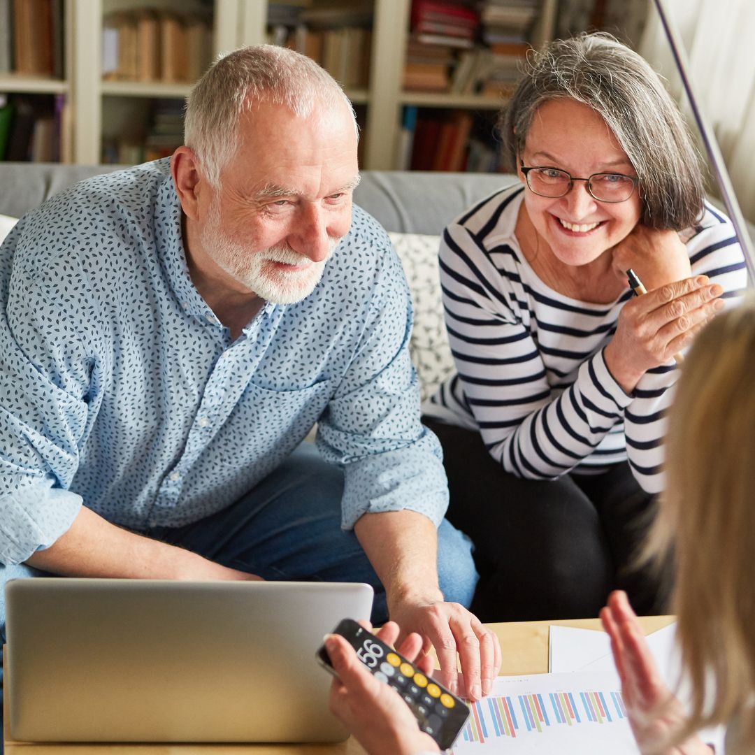 Couple reviewing documents with a person, laptop and remote. Smiling, indoors.