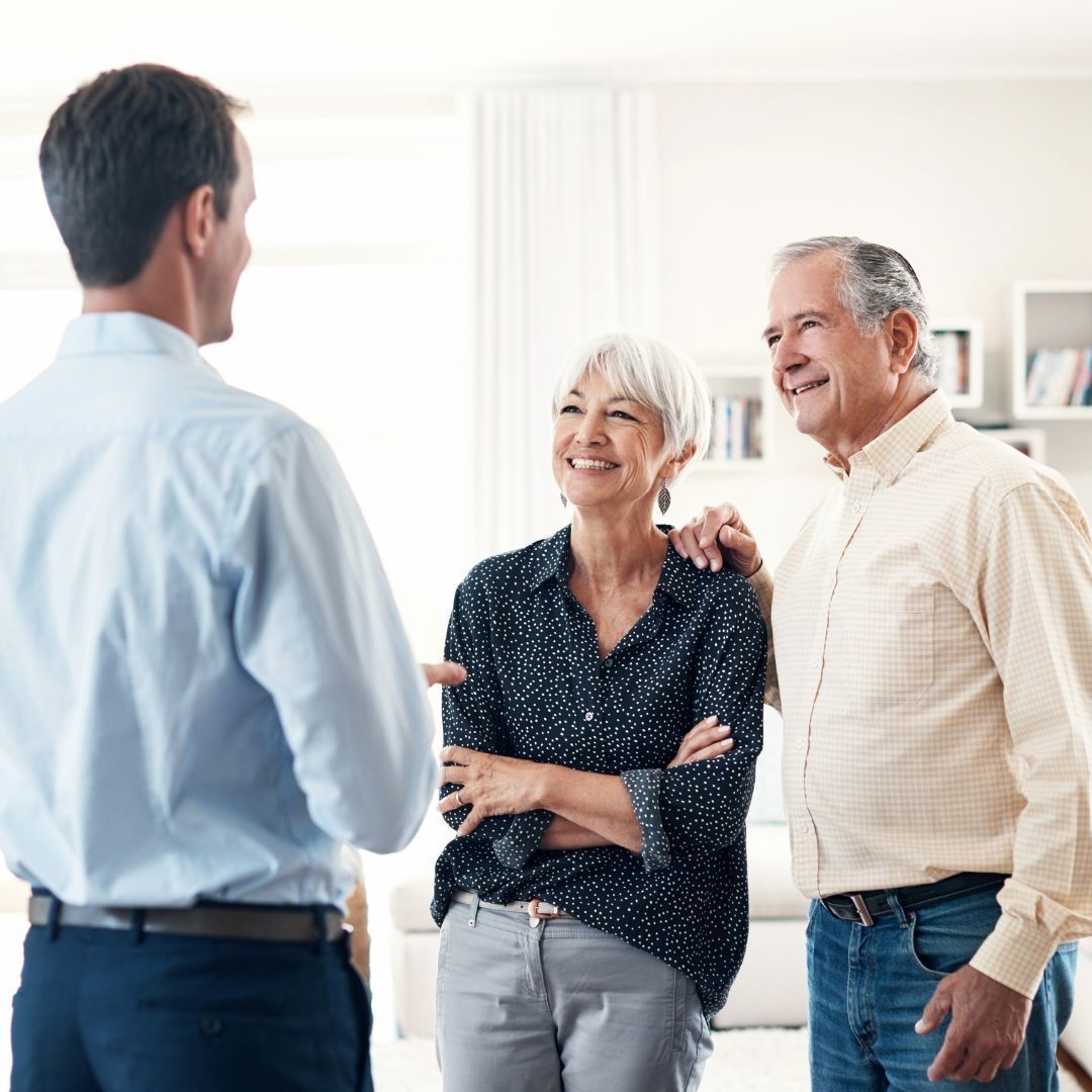 Man in blue shirt speaks to smiling couple indoors.
