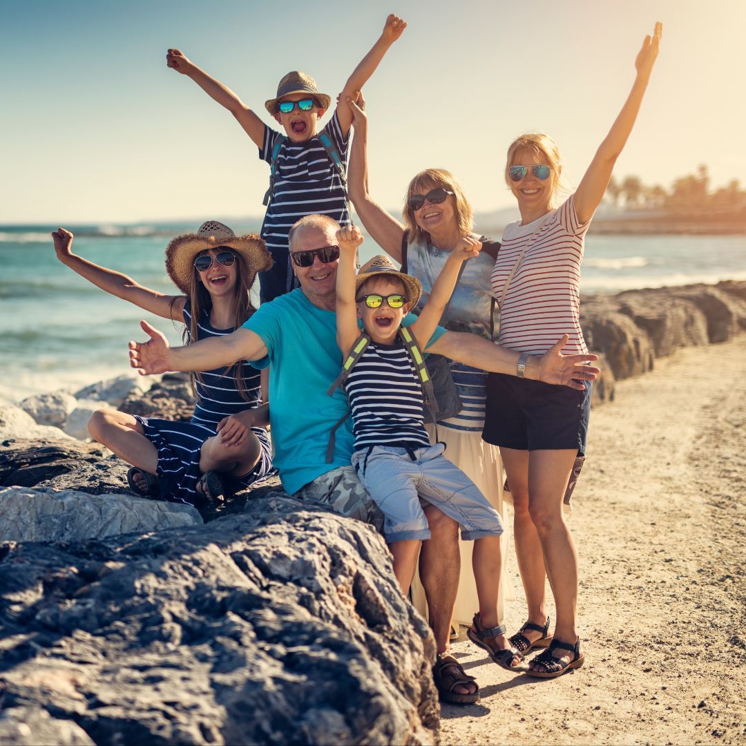 Family on a beach, arms raised in celebration. Sunny day, ocean background.