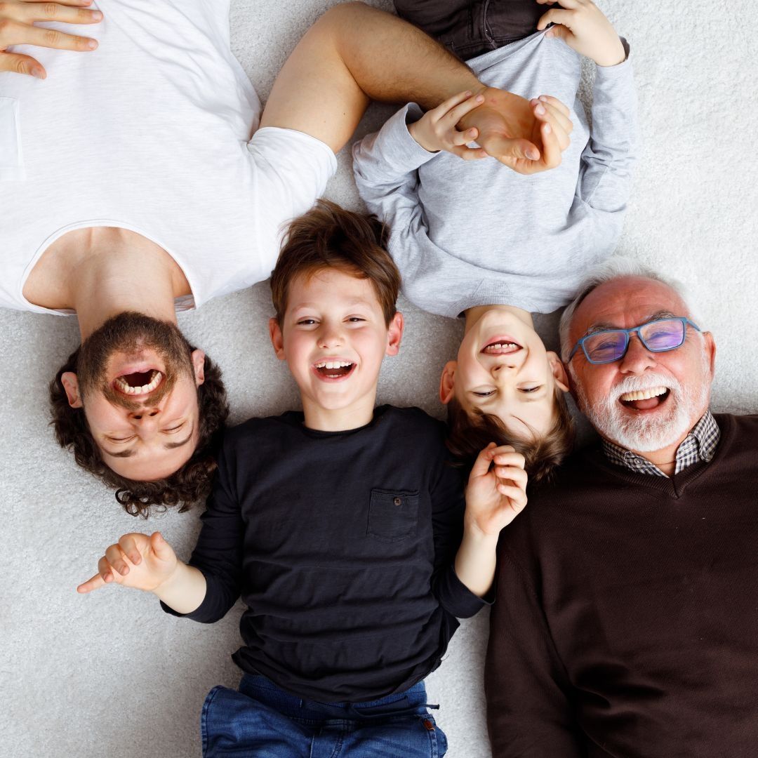 Family of four smiling and lying down on floor; white and grey clothing.