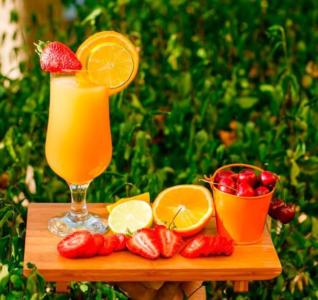 A glass of orange juice with strawberries and oranges on a wooden table.