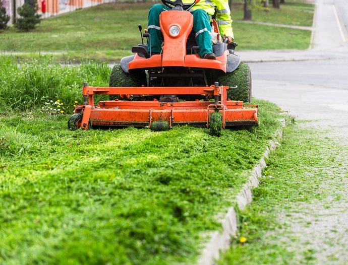 A man is riding a lawn mower on a sidewalk.