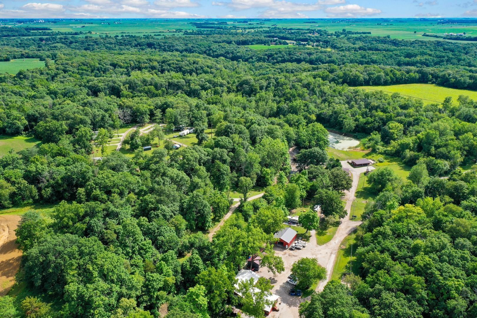 Aerial view of a rural property with a house, a red barn, and outbuildings nestled within a large, dense forest.