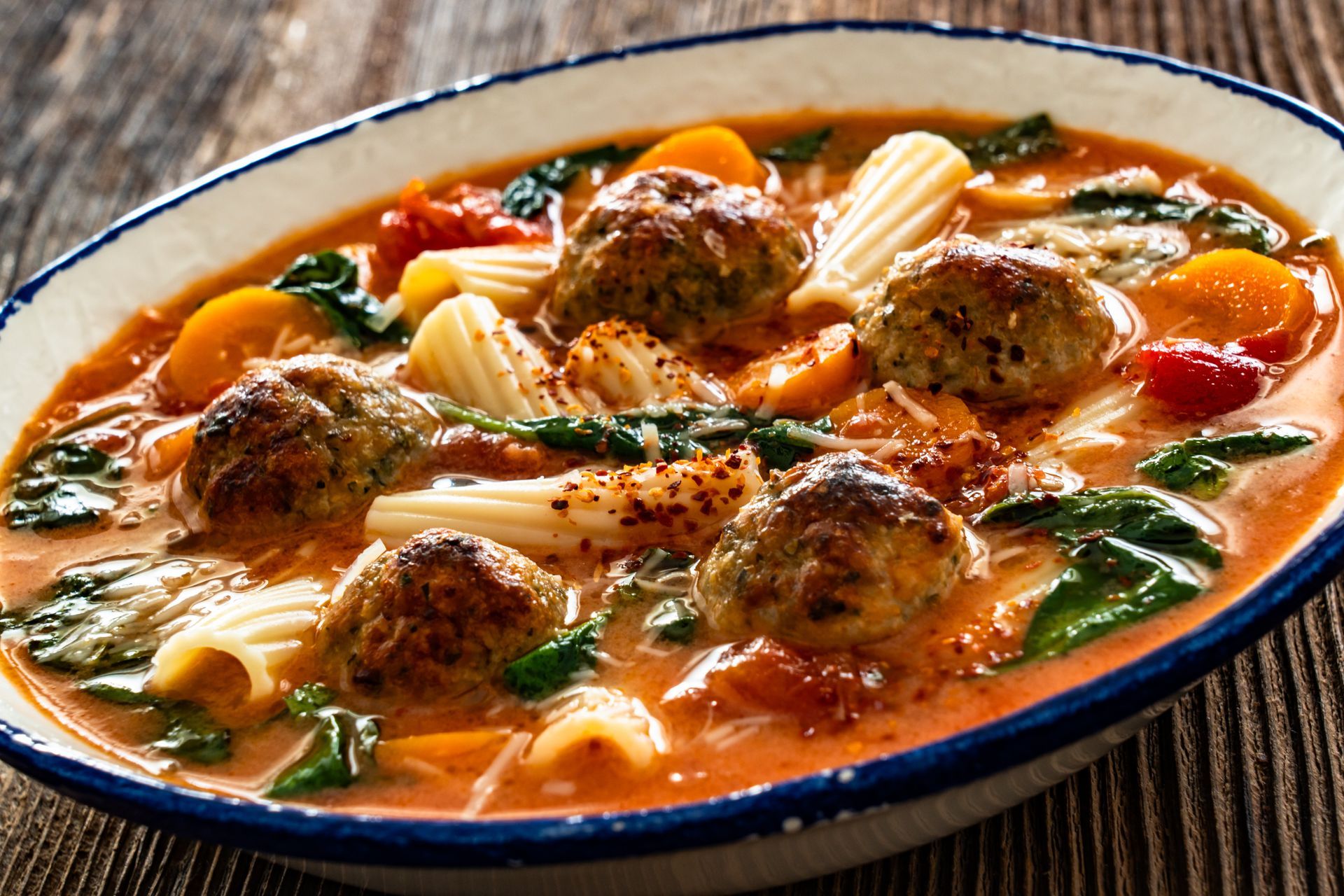 A bowl of Italian wedding soup containing meatballs, pasta, and spinach in a savory tomato-based broth.