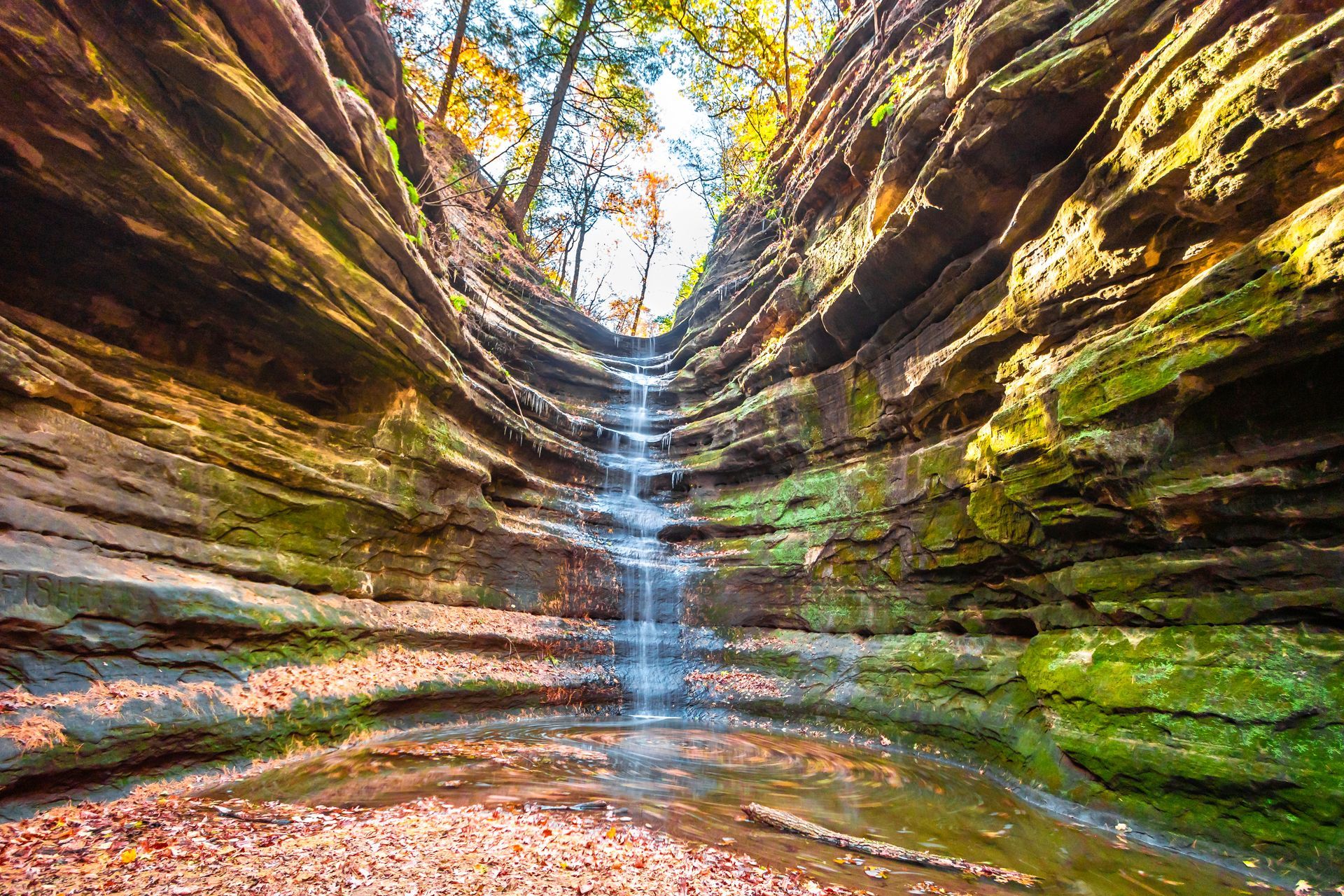 Waterfall cascading down a rocky cliff, surrounded by trees with yellow and green leaves.