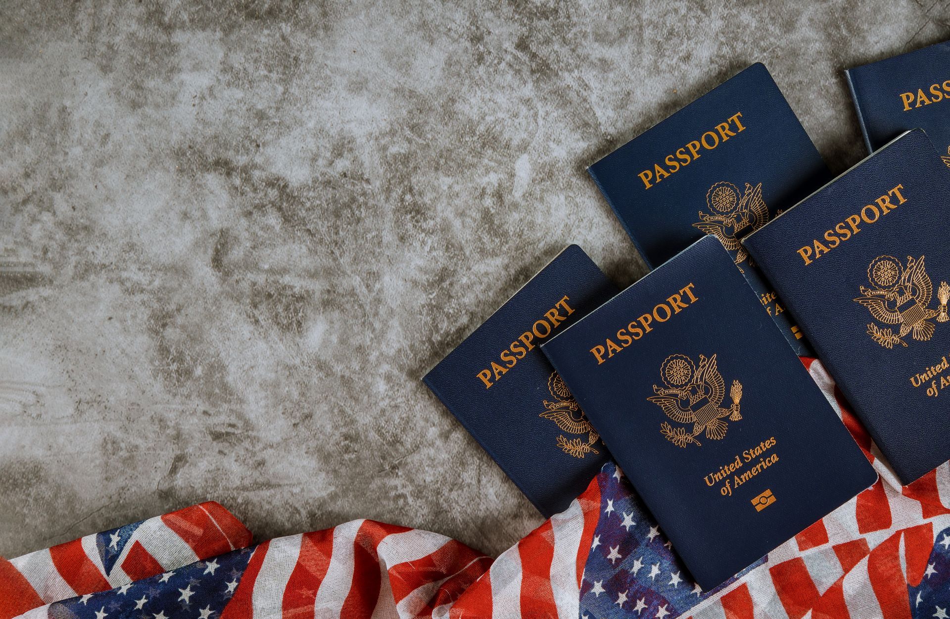 Blue US passports arranged with the American flag on a textured gray surface.