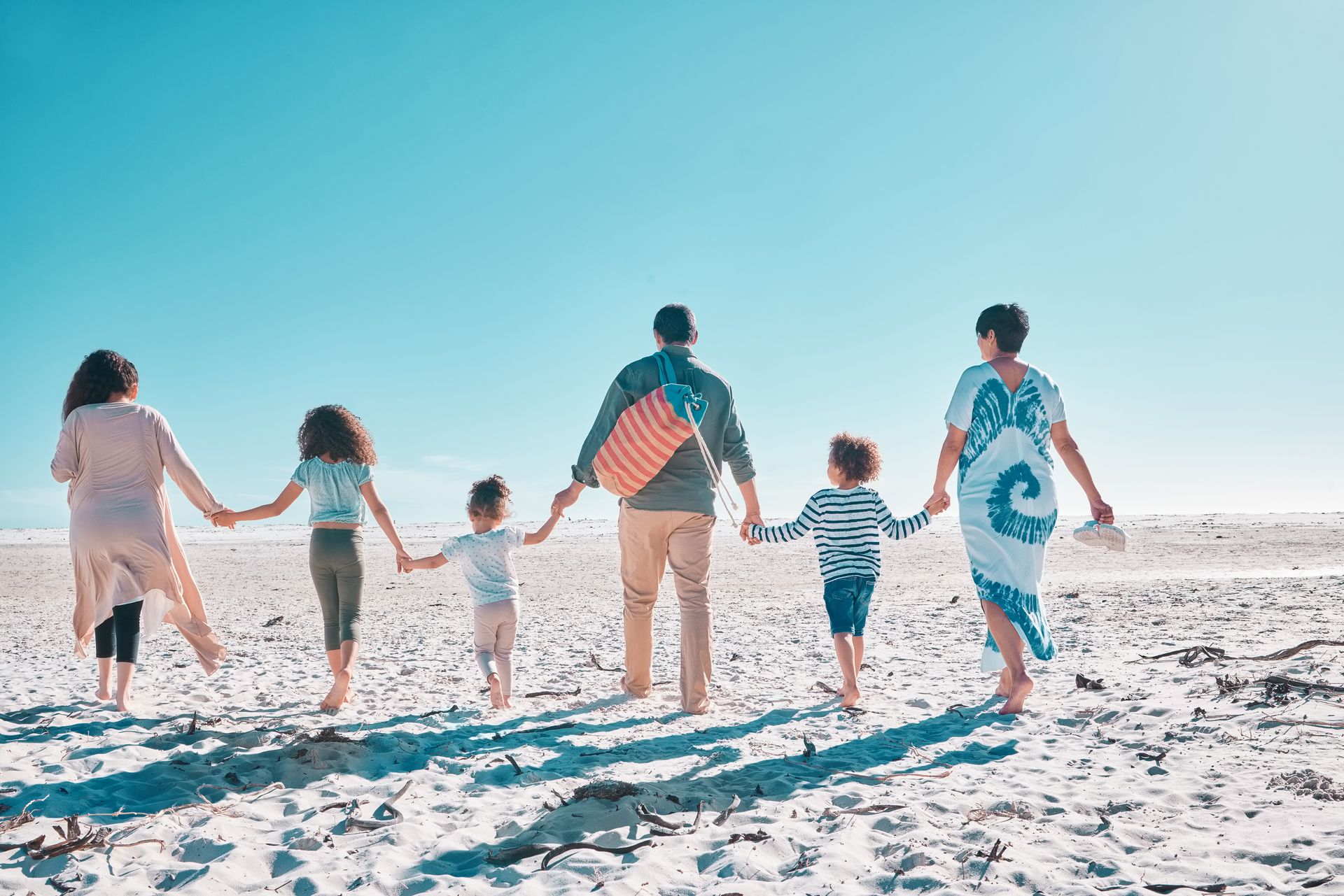 A family is walking on the beach holding hands.