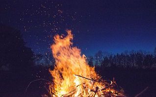 Large campfire blazing outdoors at dusk against a dark blue sky