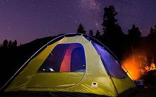 Yellow and blue tent glowing at night under a starry sky, with a campfire in the background