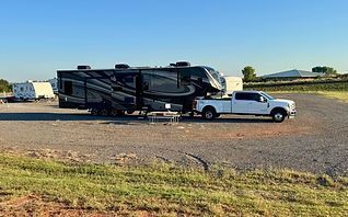White pickup truck towing a large black RV on a gravel lot under a clear sky