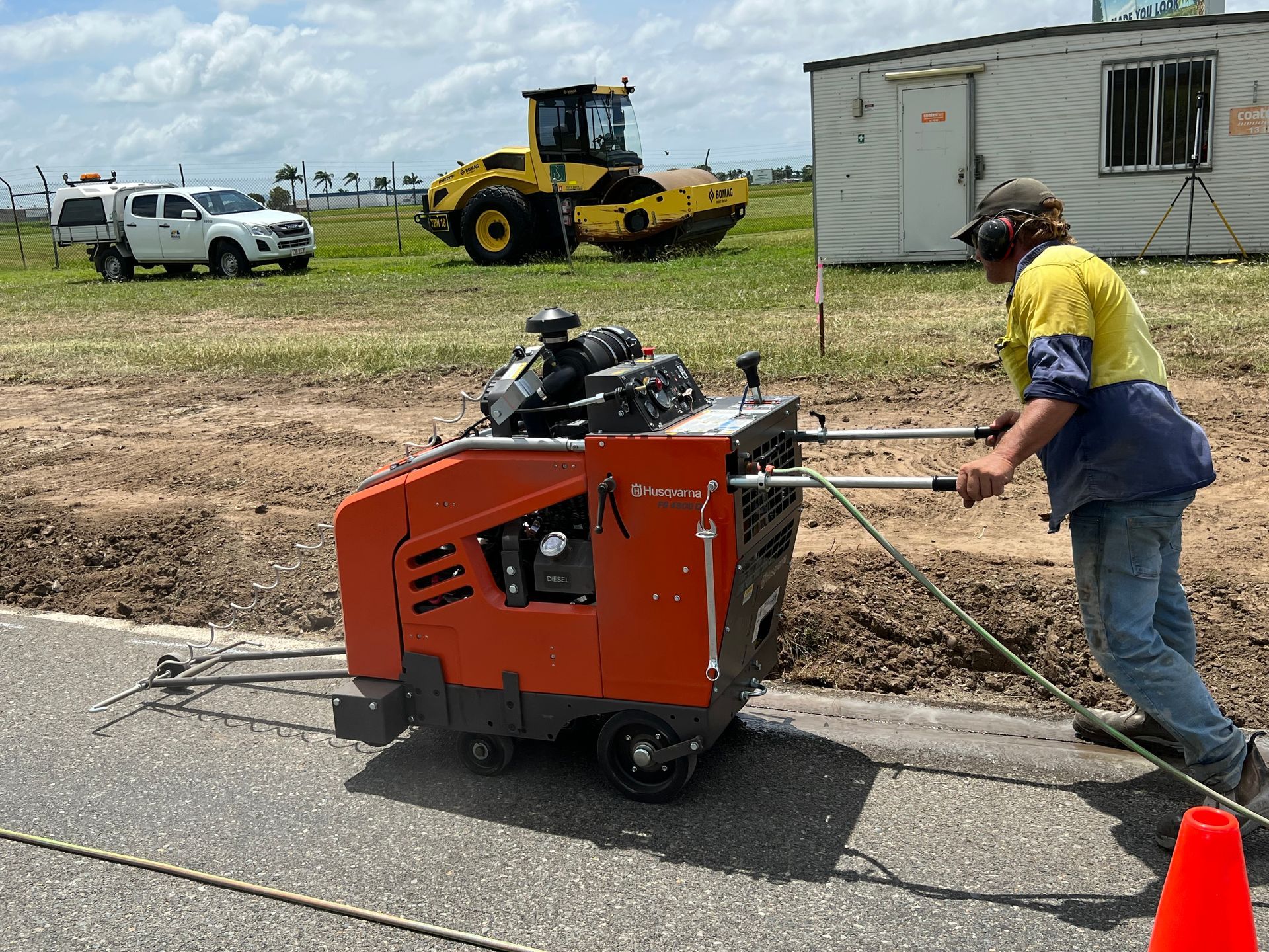 Worker pushes orange pavement saw on road beside a white trailer and yellow construction equipment. — Ablecut Concrete Cutting & Coring In East Mackay, QLD