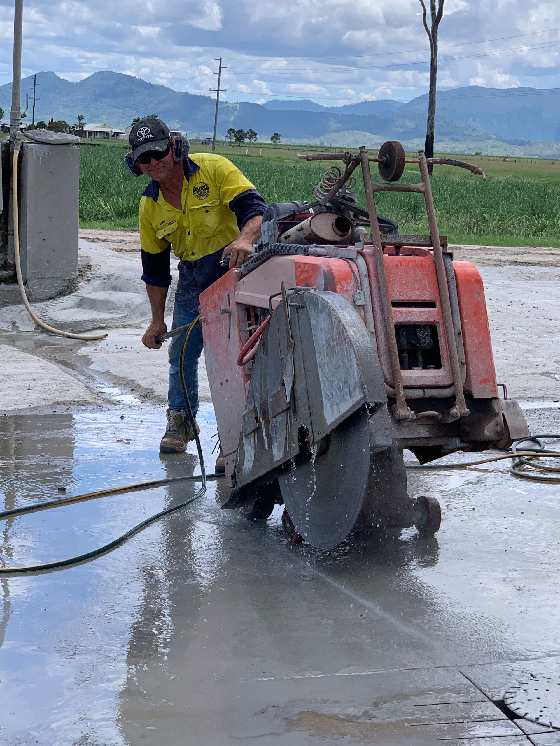 Construction worker using a concrete saw on a sidewalk, next to orange cones on a street— Ablecut Concrete Cutting & Coring In Marian, QLD