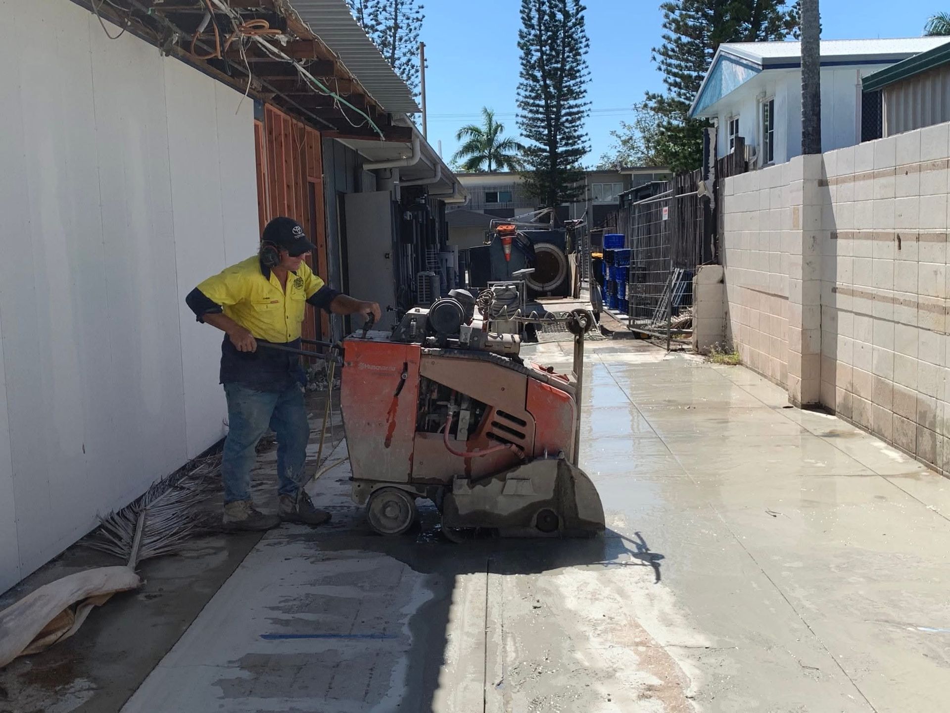 Worker beside concrete saw in a narrow alley with wet pavement and construction barriers — Ablecut Concrete Cutting & Coring In East Mackay, QLD