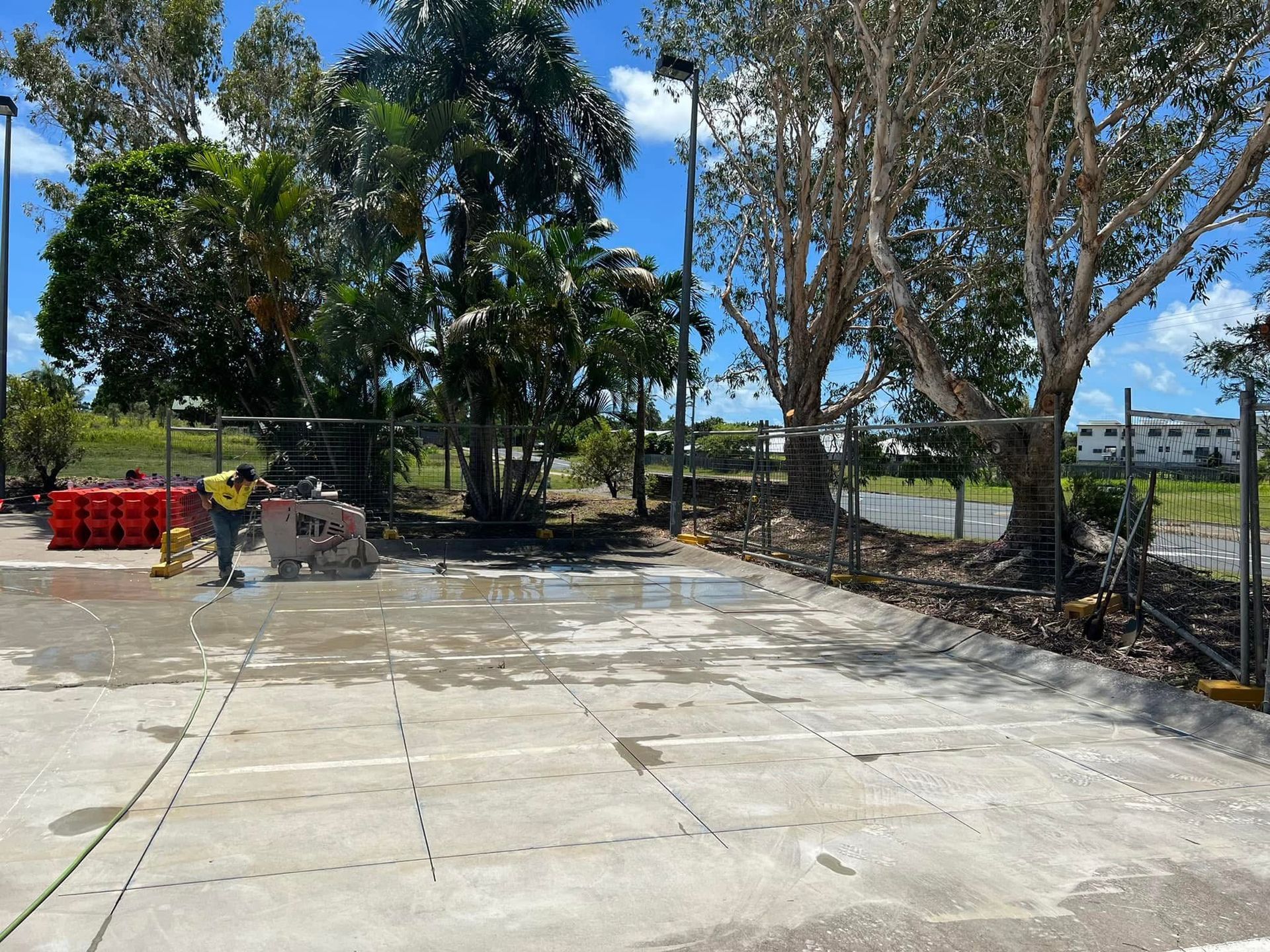 Concrete lot with trees, stacked red bins, and a fenced waterfront under a bright blue sky — Ablecut Concrete Cutting & Coring In East Mackay, QLD