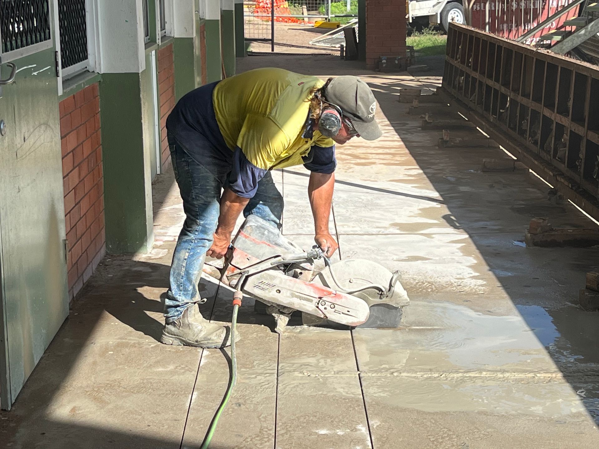 Two workers cutting pavement with a circular saw on a sidewalk under a covered walkway — Ablecut Concrete Cutting & Coring In East Mackay, QLD