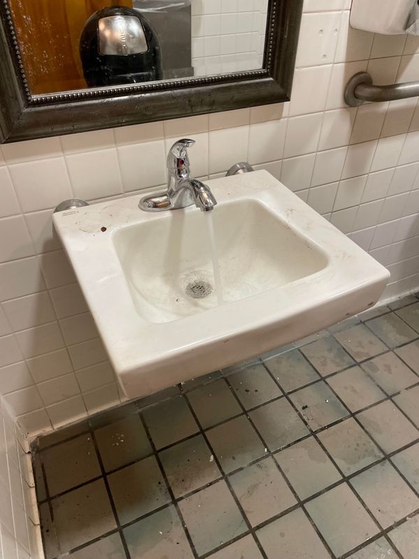 White bathroom sink with running water, mounted on a wall with tiled floor.