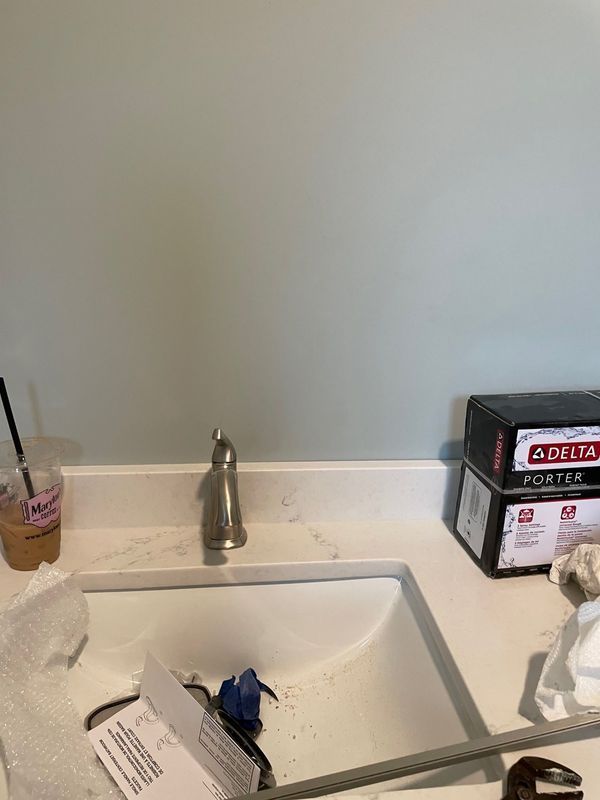Bathroom sink with faucet, white countertop, Delta faucet box, and coffee cup.