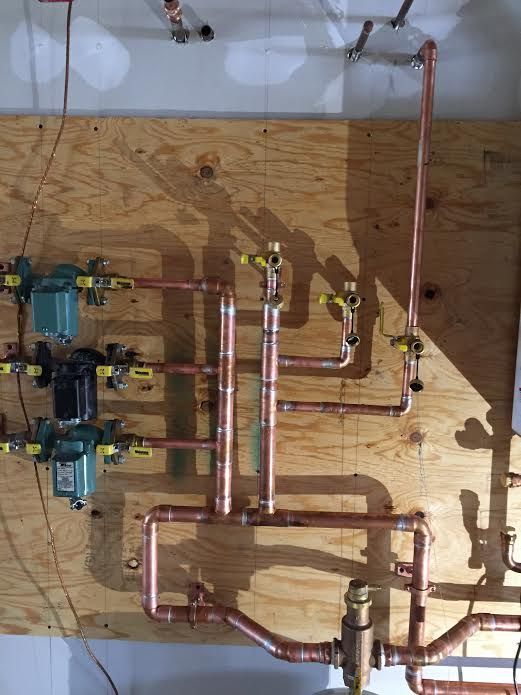 Copper pipes and valves on a wood panel, forming a plumbing system.