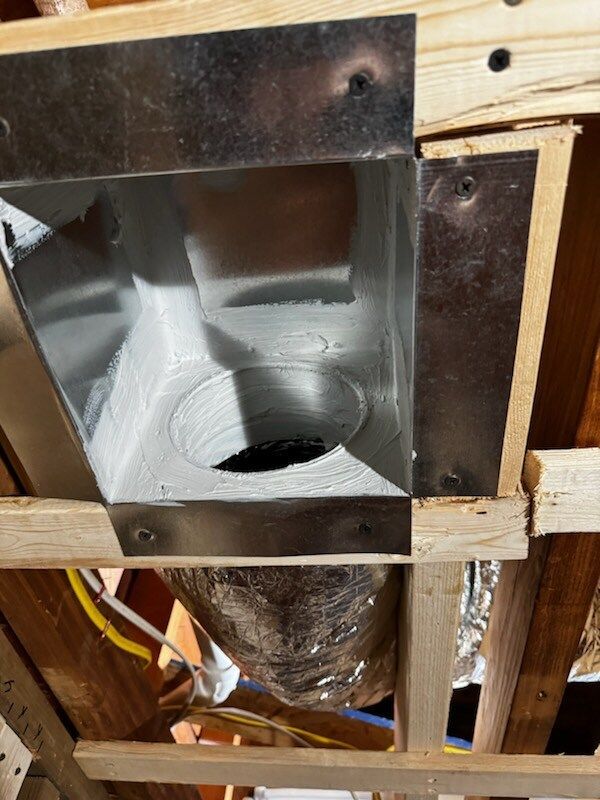 Metal HVAC ductwork installed in a wooden ceiling frame, with an insulated flex duct attached.