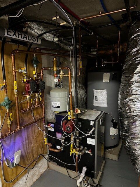 Copper pipes and various heating components in a basement. A water heater and exhaust duct are also visible.