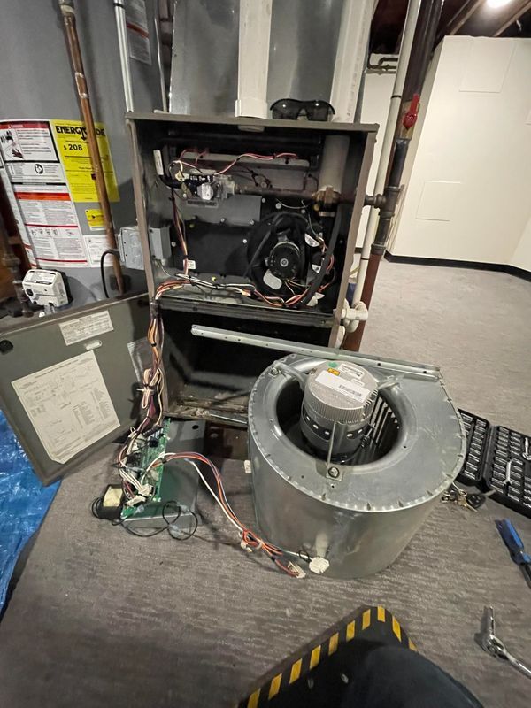 Furnace components disassembled on a floor.  A blower and control panel sit beside the open unit in a basement.
