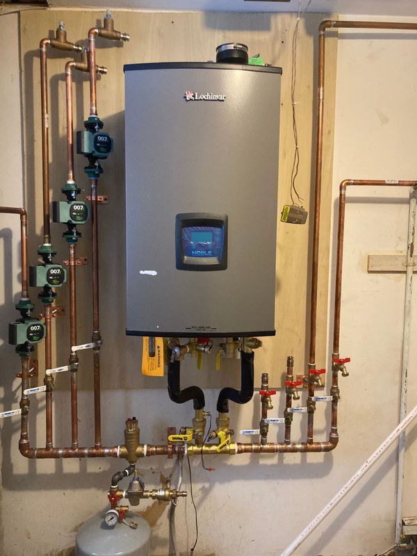Gray tankless water heater with copper pipes and valves on a beige wall.