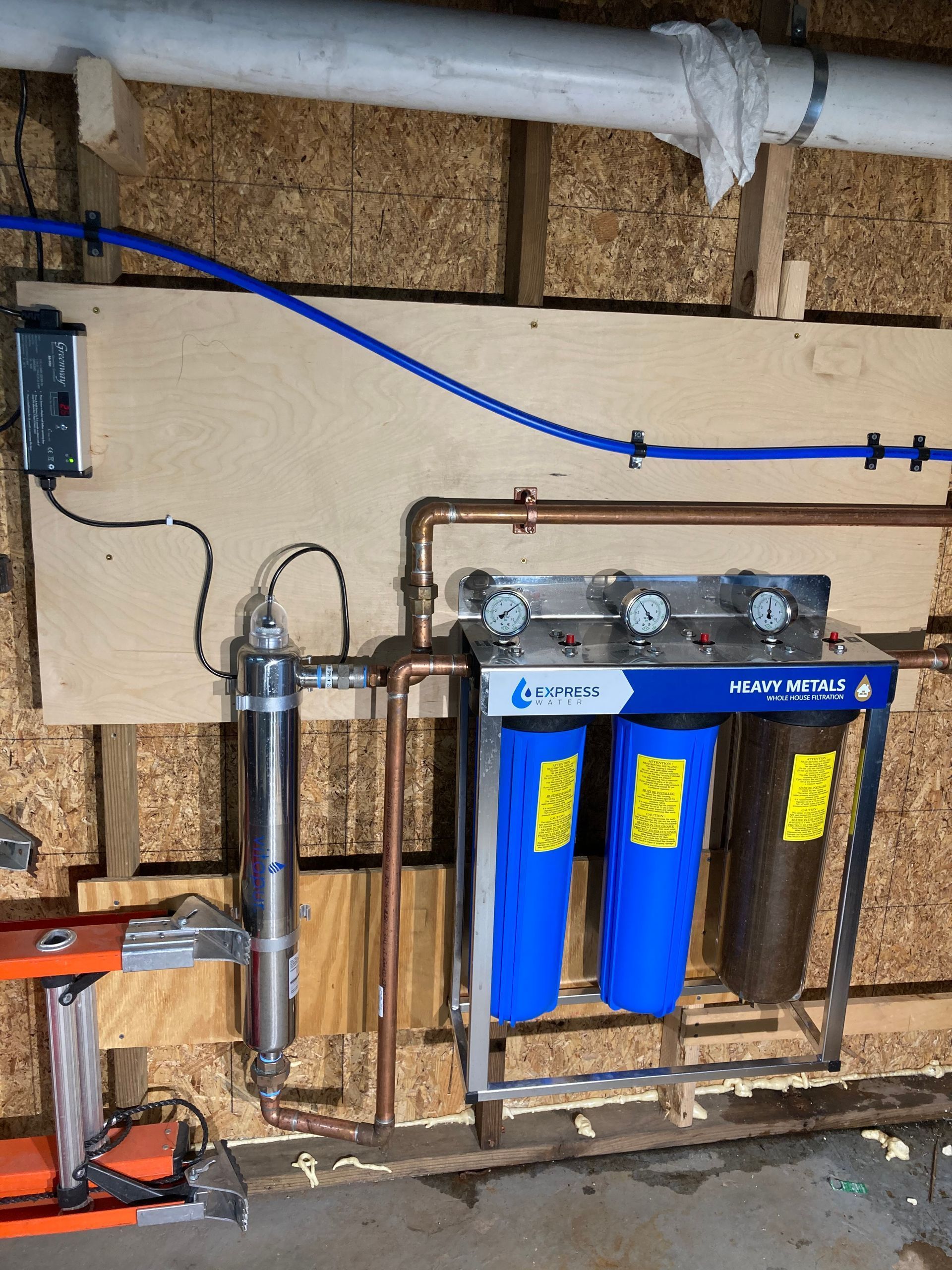 Water filtration system with three filters and copper pipes installed on a wooden wall.