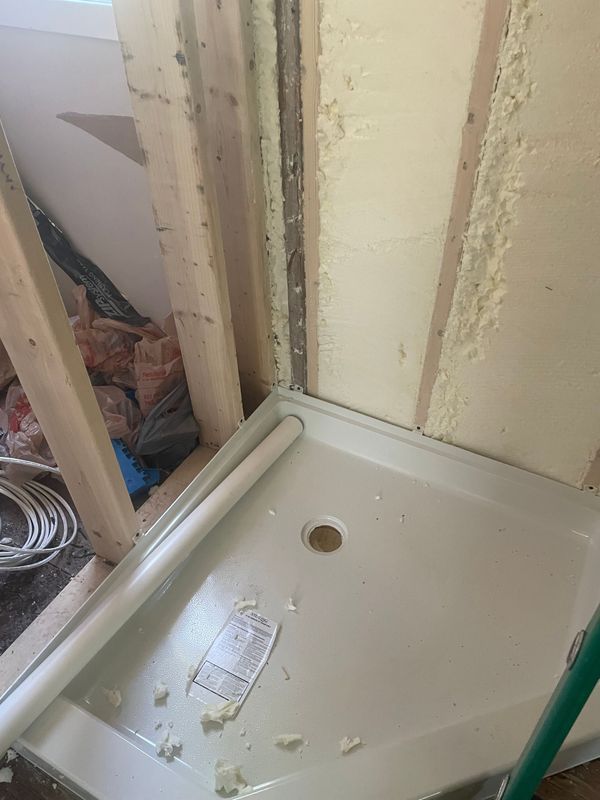 Shower pan in a construction setting, next to wooden studs and insulation.