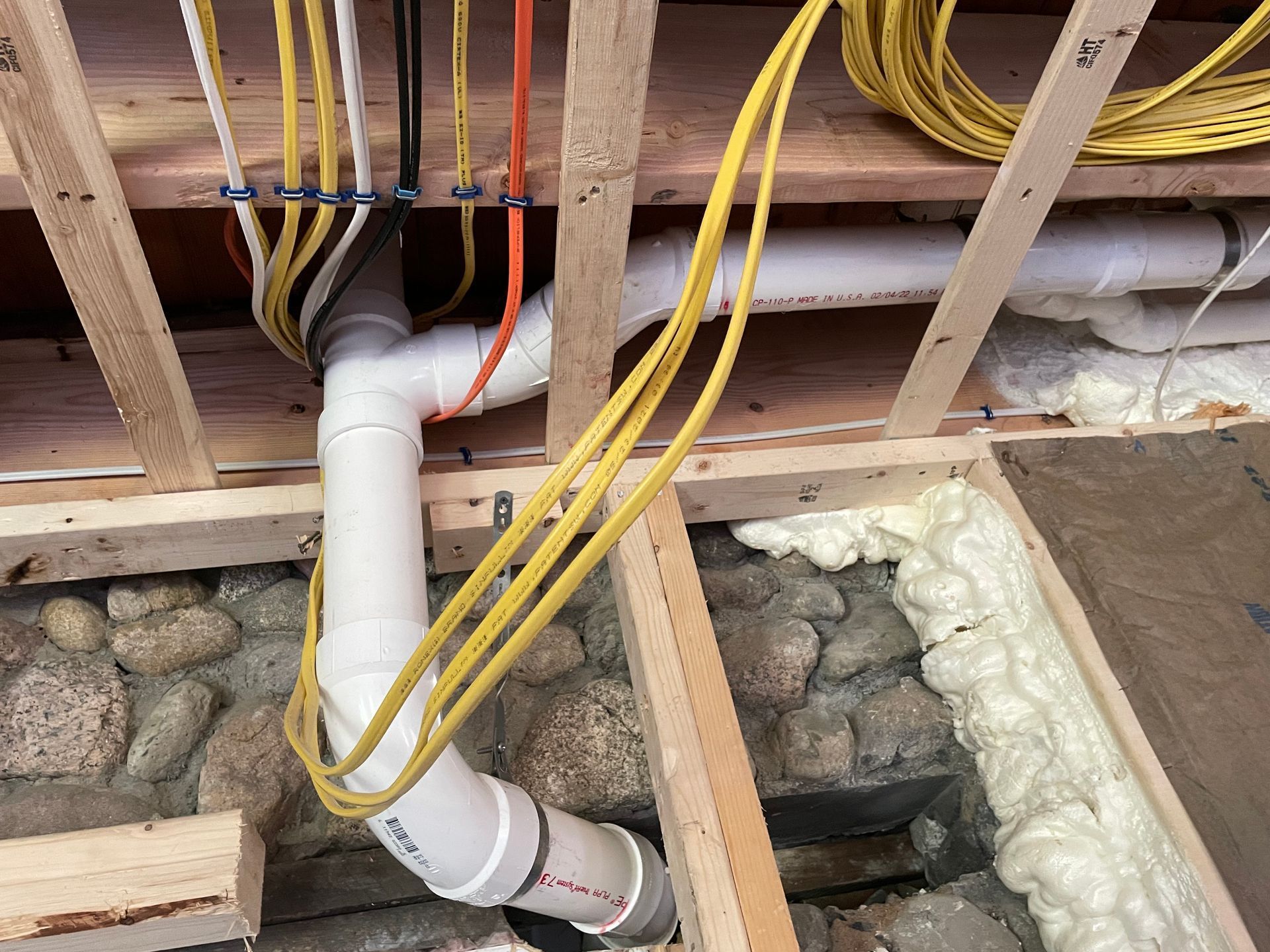 Plumbing and electrical work in a wooden framework, with white pipes and yellow wires.