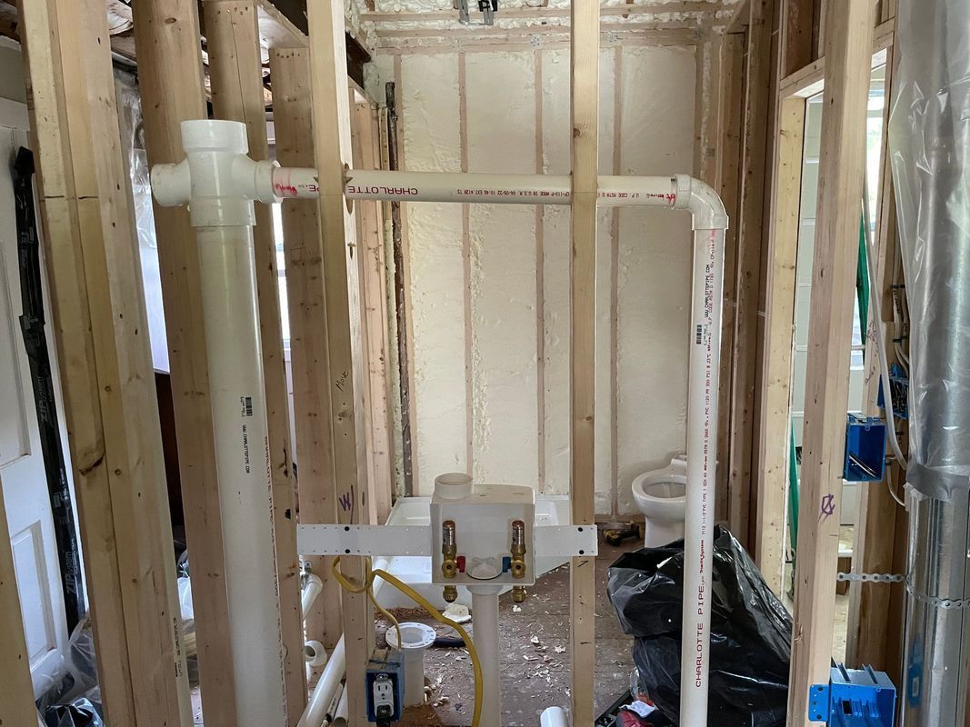Interior view of a bathroom under construction with exposed framing, plumbing, and a toilet.