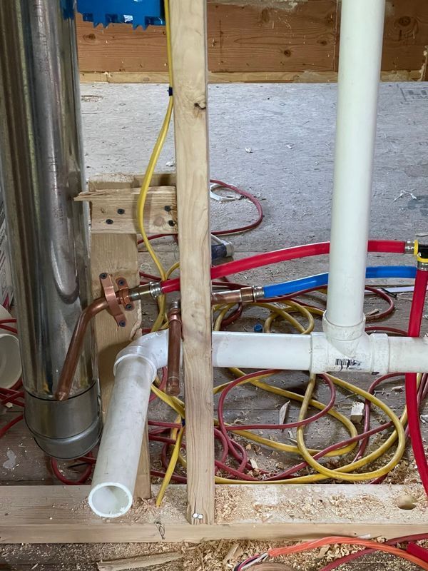 Plumbing and electrical work in a construction setting. Pipes, wires, and a water heater are visible.