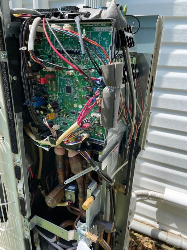Open outdoor unit, showcasing interior components, wires, and circuit boards. Copper tubing and insulation visible.