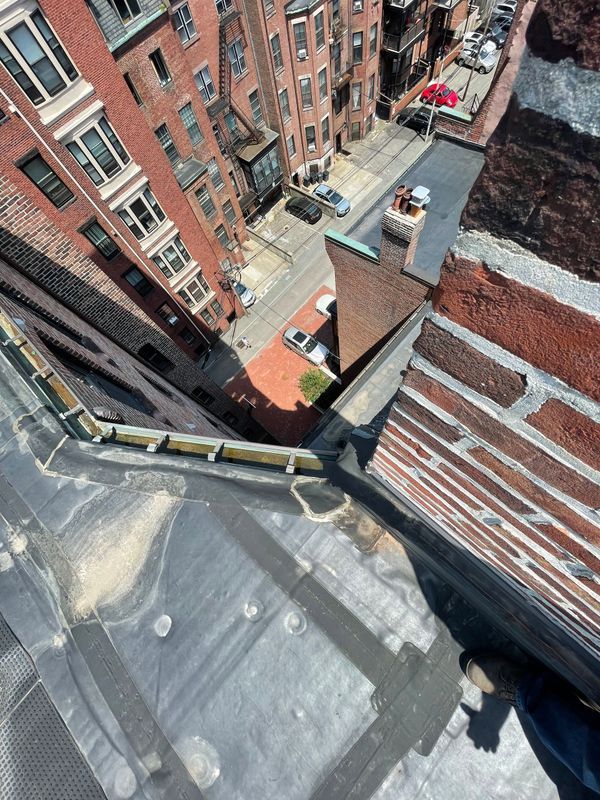View from a rooftop, looking down at a street with brick buildings and a red umbrella.