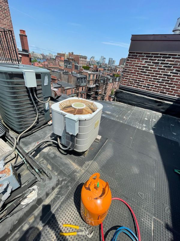 Rooftop scene with two air conditioning units, orange tank, and city skyline.