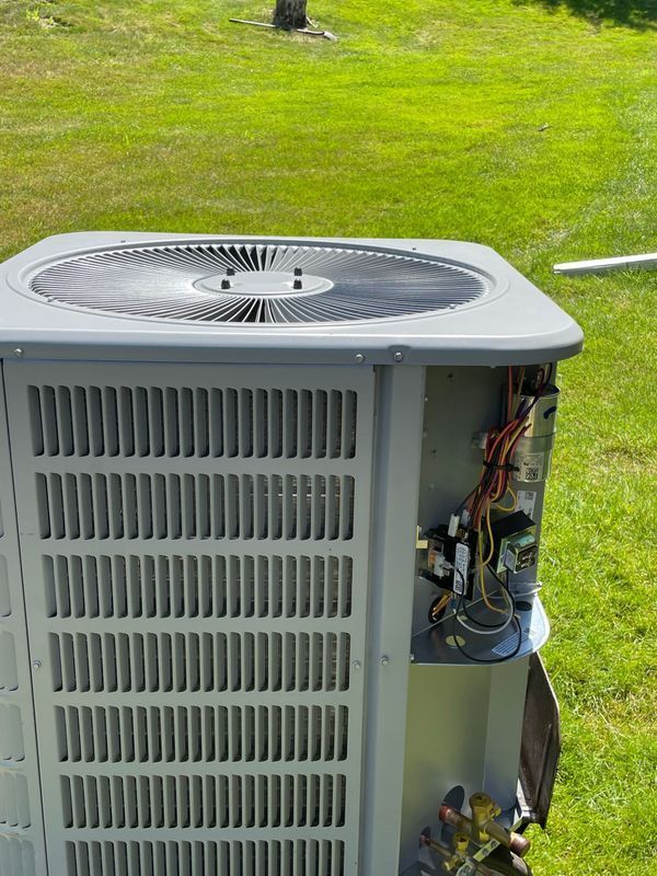 Outdoor air conditioning unit with open side, revealing electrical components against green grass.