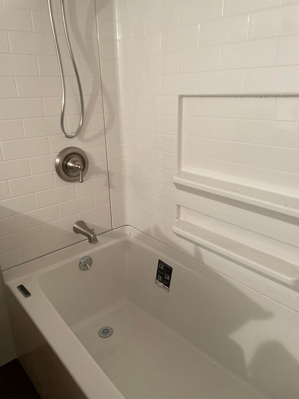White bathtub and shower with subway tile, built-in shelf, and silver fixtures.