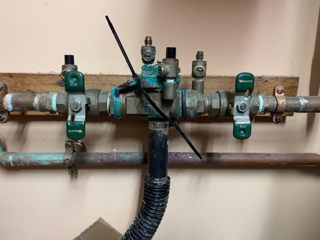 Copper pipes and valves, with green handles, connected to a central unit secured by a zip tie.