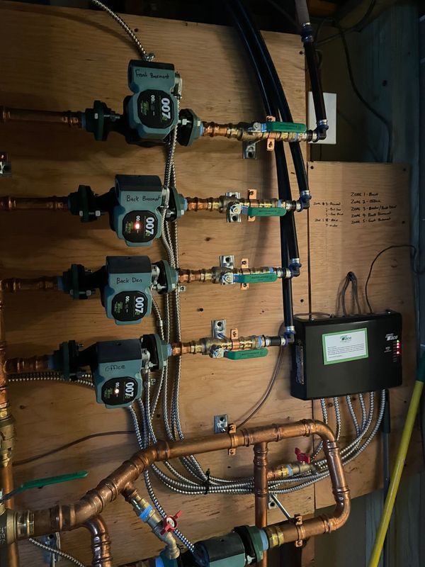 Hydronic heating system with copper pipes, pumps, and control panel on a wooden board.
